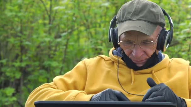 Vieil homme dans les écouteurs et les types de gants stériles sur ordinateur portable — Video