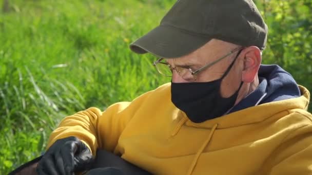 Oudere man in bril en masker types op notebook in de tuin — Stockvideo