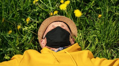 Siyah maskeli yaşlı adam yeşil çimlerin üzerinde yatıyor.