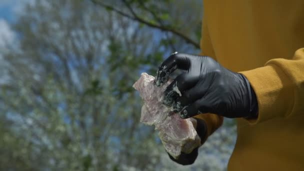 Человек в черных перчатках вставляет маринованное мясо на шампур — стоковое видео