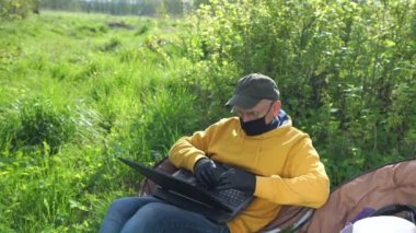 Steril maskeli yaşlı bir adam ve siyah dizüstü bilgisayarda eldivenli tipler.