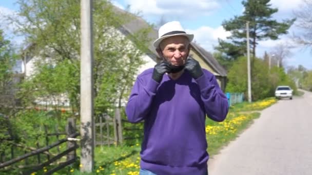 Pensionär i mask promenader längs byn gatan närbild — Stockvideo