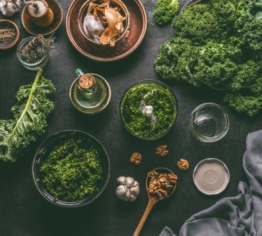 Koyu renk mutfak masasının arka planında pesto için malzemelerle birlikte kale yaprakları var. Kale pesto hazırlığı. Sağlıklı detoks sebzeleri. Temiz yemek ve diyet konsepti. Vejetaryen yemeği.