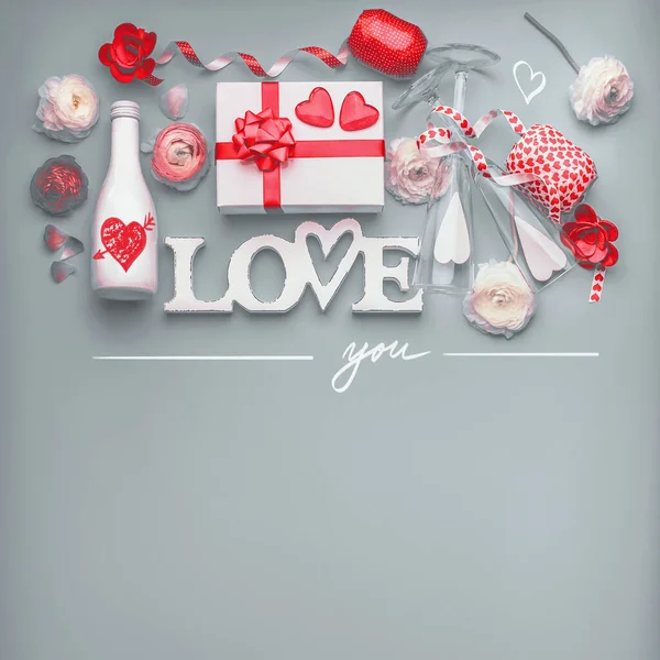Valentines day background . Festive composition of love made with flowers, gift box and red bow, bottle of champagne with glasses, hearts and party accessories. Love you message. Flat lay,  Border