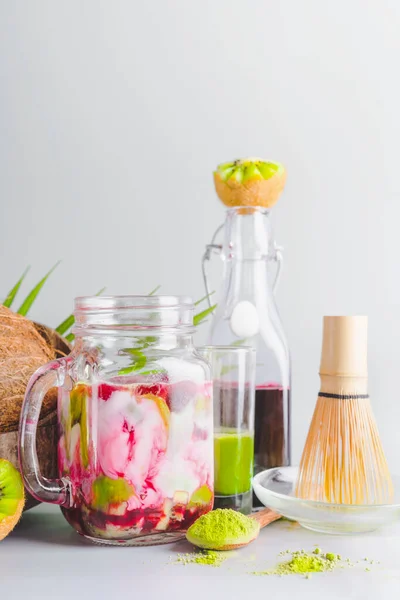 Trendy matcha green tea latte in glass jar with ingredients. Matcha espresso fusion drink with pink fruits juice. Healthy antioxidants, detox and weight loss beverage. Vegan summer food. Close up