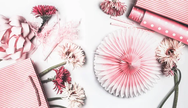 Flat lay of pink accessories to various female holidays: Mothers day , Womens day, birthday or wedding. Paper shopping bag with flowers,paper, party fan and ribbon on white background, top view