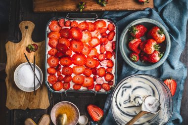 Çilekli pasta, kırsal mutfak masasında taze böğürtlenler, kaseler, kesim tahtası, şeker ve krema, üst manzara.