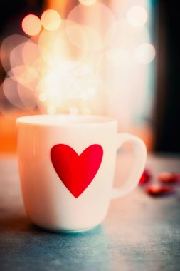 Bokeh ışıklandırma arka planında kırmızı kalpli rahat bir kupa. Aşk sembolü ya da Sevgililer Günü konsepti