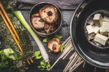 Asya çorbası için yemek malzemeleri: udon eriştesi, tofu, Shiitake mantarı, nori ve yeşil soğan koyu kırsal arka planda, üst manzara