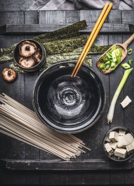Pişirme malzemeleri ile Miso çorbası hazırlama: udon eriştesi, tofu, Shiitake mantarı, nori ve yeşil soğan koyu kırsal arka planda, üst manzara