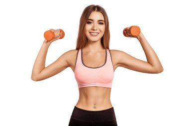 Ellerinde turuncu halterler tutan, gülümseyen, bisepsi pompalayan, omuzları için egzersiz yapan güzel genç bir kadın. Atletik vücutlu. Beyaz, izole edilmiş arkaplan.