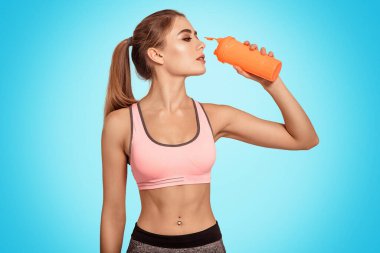 Güzel bir kadın spor bardağından su içer. Yarışmaya hazırlanın. Spor malzemeleri, beslenme ve protein kullanın. Eğitime susamışım. Mavi arkaplan.