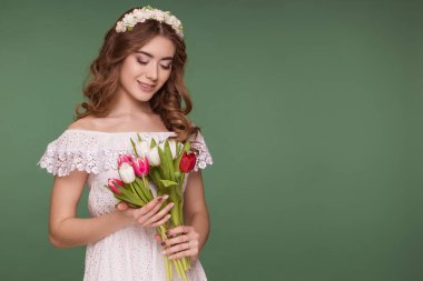 Güzel bir genç kadın mor bir arka planda duruyor, beyaz bir elbise ve başında bir çiçek çelengi ve bir buket lale ile. Uluslararası Kadınlar Günü, 8 Mart.