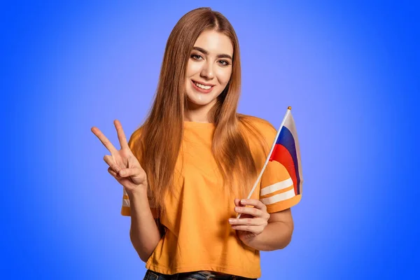 A beautiful young woman holds in her hands the flag of Russia and shows the sign Victoria, Peace, Pacif. Exchange student learning a foreign language. Tourist traveling.