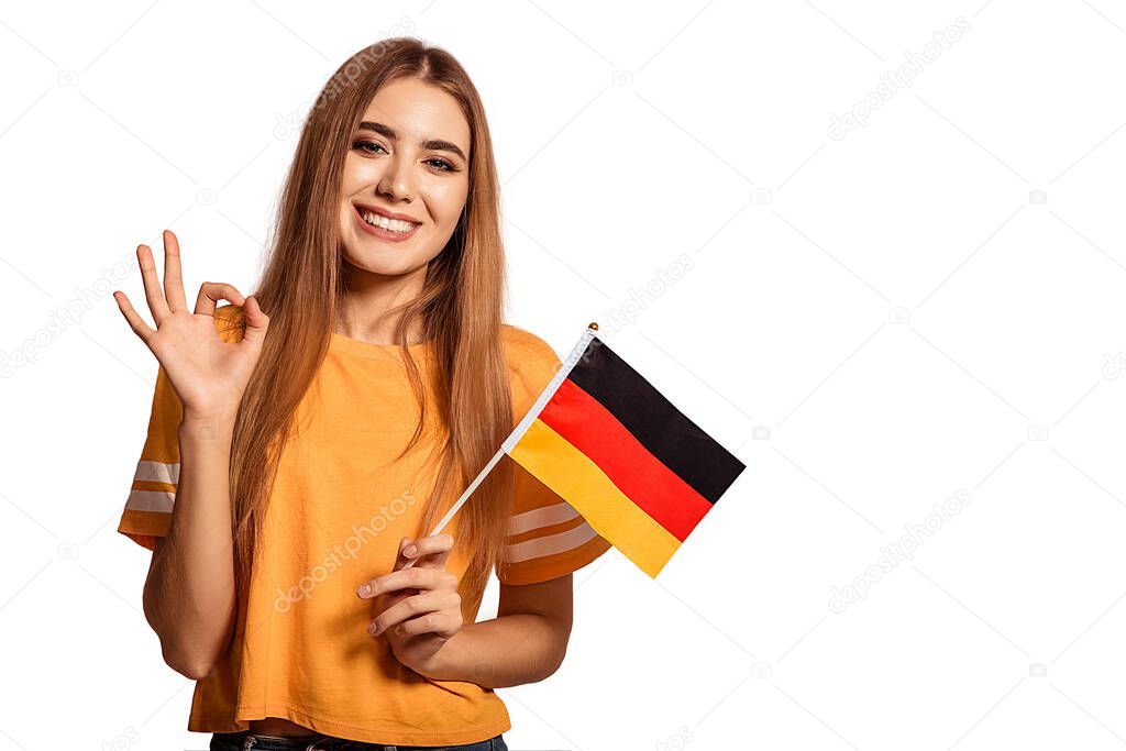 A beautiful young woman holds in her hands the flag of Germany and shows the OK sign. Exchange student, learn Germanic language. Tourist traveling. White background. Isolate. Football fan.