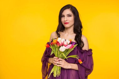 Sarı arka planda elinde bir buket lale tutan güzel esmer kadın. Mor, ince elbiseli bir kadın. 8 Mart, Matri Günü..
