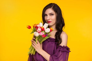 Sarı arka planda elinde bir buket lale tutan güzel esmer kadın. Mor, ince elbiseli bir kadın. 8 Mart, Matri Günü..