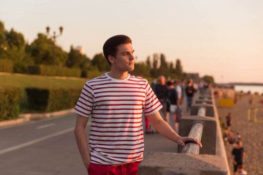 Yakışıklı, genç bir adam, beyaz çizgili gömlekli bir adam bir köprüye yaslanıyor ve uzaklığa bakıyor. Baraj, sahil kenarı. Yaşam tarzı. Eski filmlerden bir karakter.