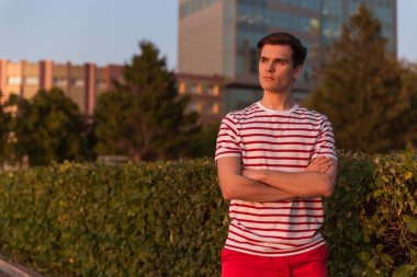 Yakışıklı, genç bir adam, beyaz çizgili tişörtlü ve şortlu bir adam parkta yürüyor. Temiz havada yürü. Milyonlarca, Z. kuşağı yaşam tarzı..