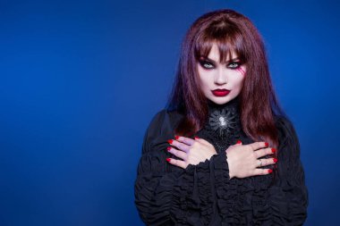 Güzel bir kadın, bir vampir, bir cadı, ölü bir adam gibi elleri göğsünde. Tabuttan çık. Cadılar Bayramı kostüm partisi. Parlak makyaj. Etiketleme için boş mavi arkaplan.