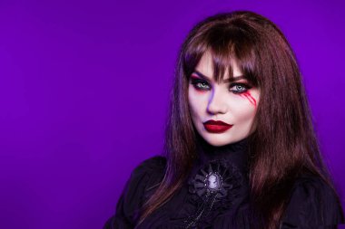 Cadı, mor arka planda siyah gotik elbiseli bir vampir. Portre. Amerikalı, Cadılar Bayramı için kostüm partisi kıyafeti. Parlak makyaj