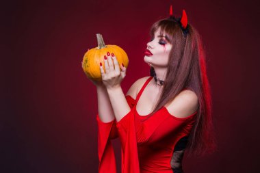 Güzel, seksi, şeytan kostümü giymiş bir kadın balkabağını öpüyor. Amerikalı, Cadılar Bayramı için kostüm partisi kıyafeti. Metnin burada.