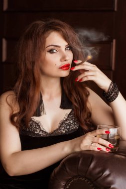 Siyah elbiseli güzel seksi bir kadın sigara içiyor ve viski içiyor. Koltuk göğüs tarlası. Hanımım, Casus Kız