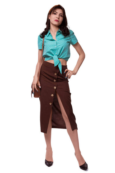 A beautiful, caucasian brunette woman in full-length, on a white background, is wearing a brown skirt and a blue blouse and is holding a small bag. Tourist, sexy domoho