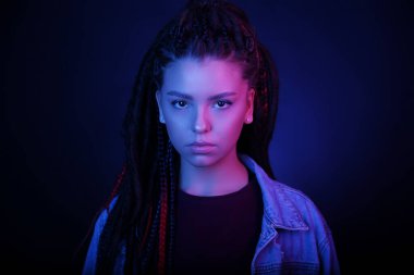 Neon pembe ve mavi ışıklı genç bir kadının mutsuz portresi. Gece kulübünde rastalı bir kız, fosforlu kalemle makyaj yapıyor. Ciddi bir yüz ifadesi. Clubber, gece hayatı konsepti.