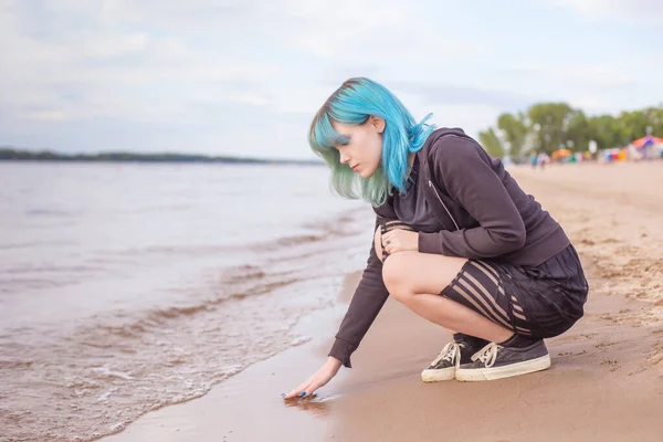 漂亮的年轻姑娘坐在沙滩上 穿着温暖的衣服接触着水温 海滩季节的开幕 这个女人的头发是蓝色和青绿色的双色头发 复制空间 Milinial — 图库照片