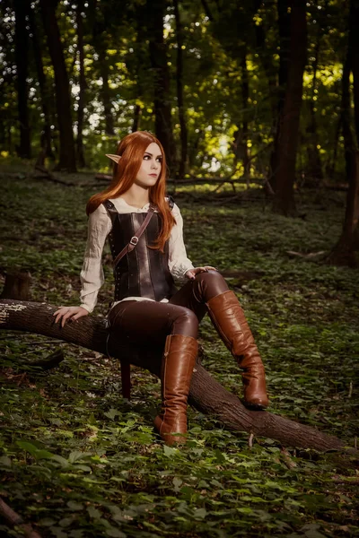 オレンジの髪と革のコルセットで 鋭い耳を持つファンタジーの女性 自己戦士は 森の中に座っています ロールプレイングゲーム コスプレ — ストック写真