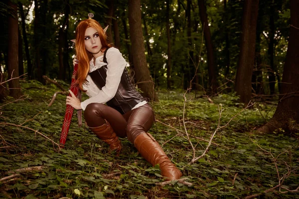 一个美丽的 年轻的女性精灵 一个锐利的耳朵 橙色头发和皮革紧身衣的战士 在森林里的狩猎 在战斗的姿态 化妆品 — 图库照片