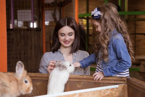 Mom and daughter in a contact zoo, fed from rabbits. The family is on the farm.