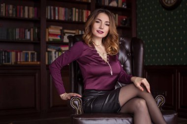 Güzel bir kadın kahverengi deri bir sandalyede oturuyor, kişisel asistanı, sekreteri. İş imajı. Flört, zigryat, ayağını yere koy..
