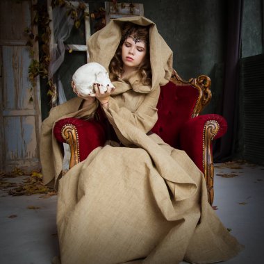 Bir prensesin ortaçağ kıyafeti, bir büyücü, kafasında başlık ve taç olan bir cadı. Antika kırmızı bir koltuğa oturuyor ve beyaz bir kafatası tutuyor. Güzel genç kız, kadınlar..