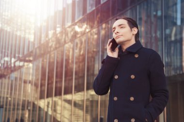 Rastalı bir adam, cam bir binanın arka planındaki akıllı telefona, telefona bakar. Modern bir şehir ve alışılmadık bir iş adamı. Sohbet sırasında, sosyal ağlarda, mesajlarda yazışmalar yapmak için..
