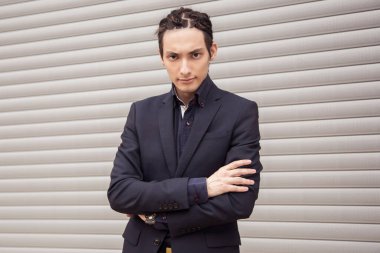 Yakışıklı genç adam gri bir arka planda ellerini çaprazladı. Kızgın, ciddi bir bakış..