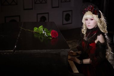 Güzel, küçük, sarışın bir kız, kırmızı, gür, yaşlı bir elbiseyle piyanonun başında oturuyor. Kadın, vampir Claudia. Japon usulü lolita, güzel kostüm. Sokak modası.