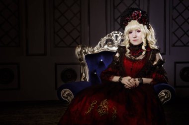 Güzel bir kadın, gür, kırmızı, gotik bir elbiseyle, elleri bağlı bir sandalyede oturuyor. Japon usulü lolita, güzel kostüm. Sokak modası. Rokoko tarzında bir vampir. Mesajın değil.