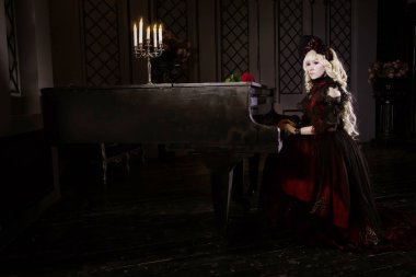 Güzel, küçük, sarışın bir kız, kırmızı, gür, yaşlı bir elbiseyle piyanonun başında oturuyor. Kadın, vampir Claudia. Japon usulü lolita, güzel kostüm. Sokak modası.