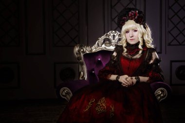 Güzel bir kadın, gür, kırmızı, gotik bir elbiseyle, elleri bağlı bir sandalyede oturuyor. Japon usulü lolita, güzel kostüm. Sokak modası. Rokoko tarzında bir vampir. Mesajın değil.