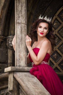 Güzel bir kadın, kırmızı elbiseli bir kraliçe, ortaçağdan kalma, merdivenlerde kemerli gümüş kartonlu, kristalli bir Gotik kapının arkasında duruyor. Kaledeki Prenses.