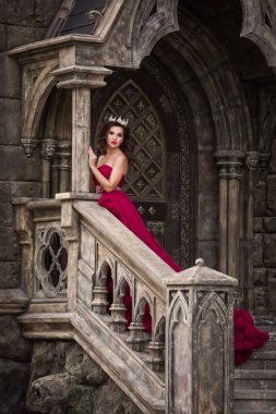 Güzel bir kadın, kırmızı elbiseli bir kraliçe, ortaçağdan kalma, merdivenlerde kemerli gümüş kartonlu, kristalli bir Gotik kapının arkasında duruyor. Kaledeki Prenses.