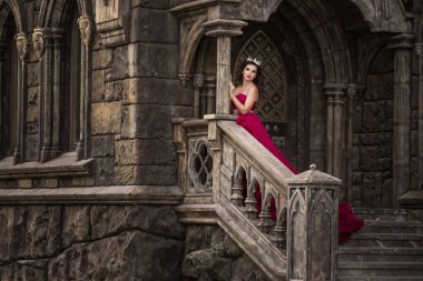 Güzel bir kadın, kırmızı elbiseli bir kraliçe, ortaçağdan kalma, merdivenlerde kemerli gümüş kartonlu, kristalli bir Gotik kapının arkasında duruyor. Kaledeki Prenses.