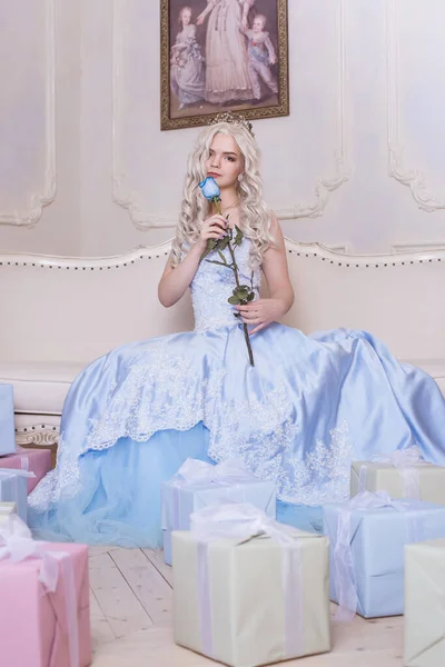 A glamorous girl, a blond woman in a crown holds a blue rose, a gift from a prince. Aroma of flowers, Cinderella, Princess in the castle. A rich queen in a dress. A lot of gifts, birthday.