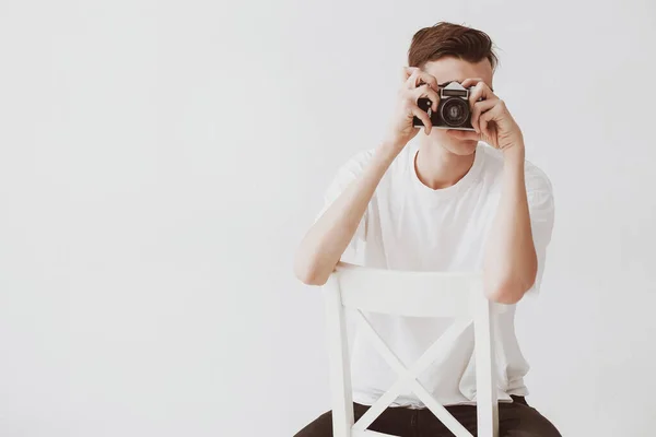 一个英俊的年轻人 用苏联的旧镜像相机拍照 手肘靠在椅子上 一个穿着白色衬裙的男人 — 图库照片