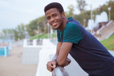 Siyahi bir adam, dirseklerini çitte okşayan bir adam, manzara gibi. Baraj, sahil. Değişim öğrencisi. Uzayı kopyala Milinial. Yakın plan portre.