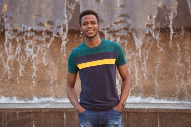 Bir zenci, modern bir şehirde bir fıskiyenin arka planında bir adam. İyi bir gülümseme. Değişim öğrencisi. Afrika, Nijerya. Eller formatta, gülümseyin..