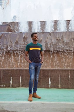 Bir zenci, modern bir şehirde bir fıskiyenin arka planında bir adam. İyi bir gülümseme. Değişim öğrencisi. Afrika, Nijerya. Eller formatta, gülümseyin..