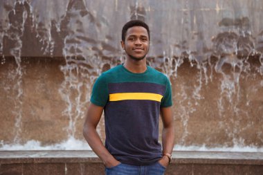 Bir zenci, modern bir şehirde bir fıskiyenin arka planında bir adam. İyi bir gülümseme. Değişim öğrencisi. Afrika, Nijerya. Eller formatta, gülümseyin..